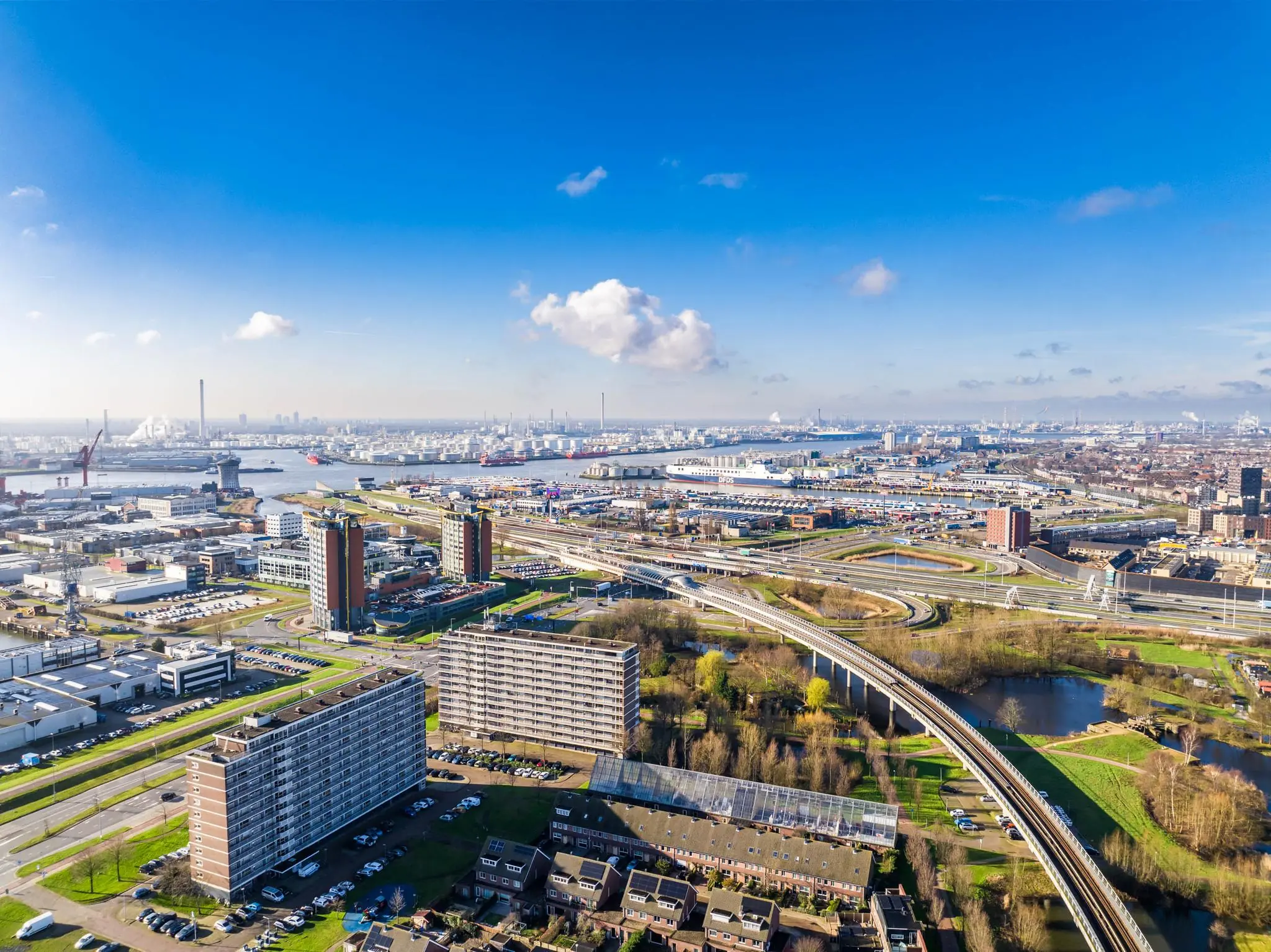Luchtfoto van de Karel Doormanweg in Rotterdam met woonwijken, wegen en industrieterrein aan de haven.